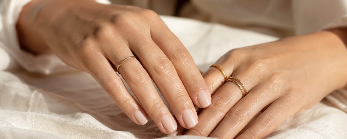 Unghie curate con manicure nude lattiginosa e mani eleganti con anelli sottili.