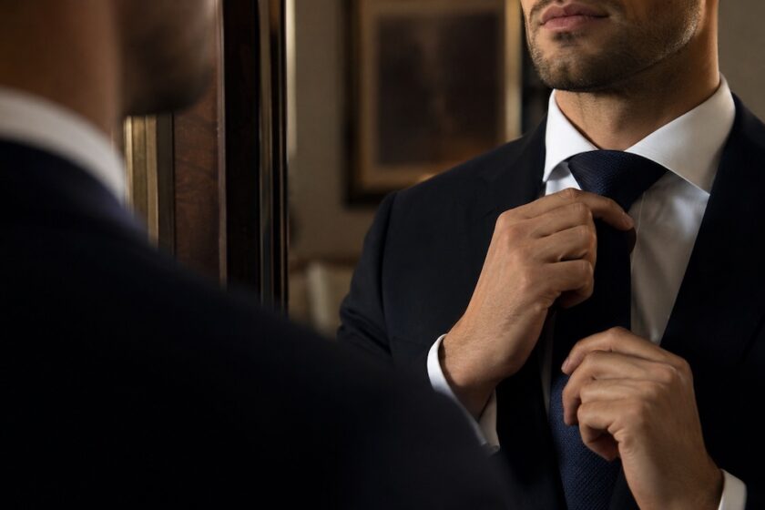 Uomo elegante che sistema il nodo della cravatta con camicia bianca e giacca sartoriale